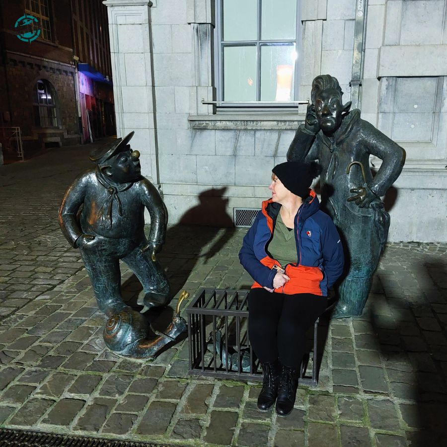 Bridget sitting between two bronze statues in a quiet evening street