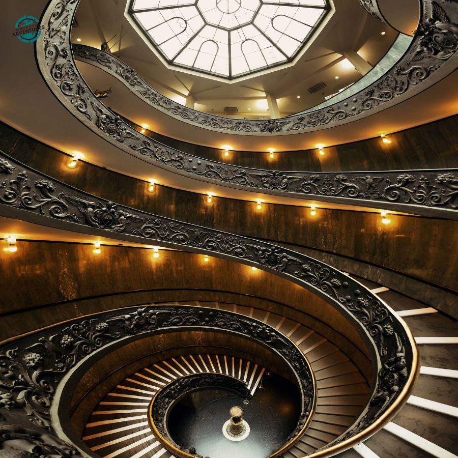 The Vatican Museum spiral staircase viewed from above, with ornate iron railings and a glass dome ceiling